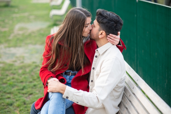 couple sitting outdoor kissing at bench